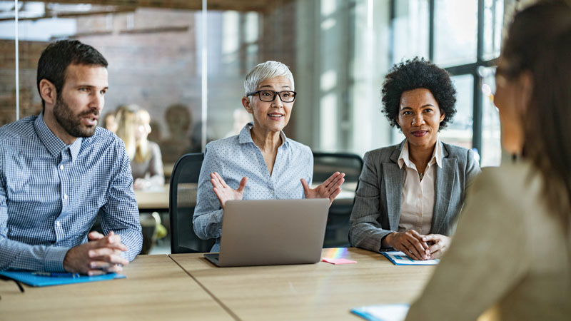 Team of business colleagues talking to their candidate during a job interview in the office. Focus is on happy senior woman.