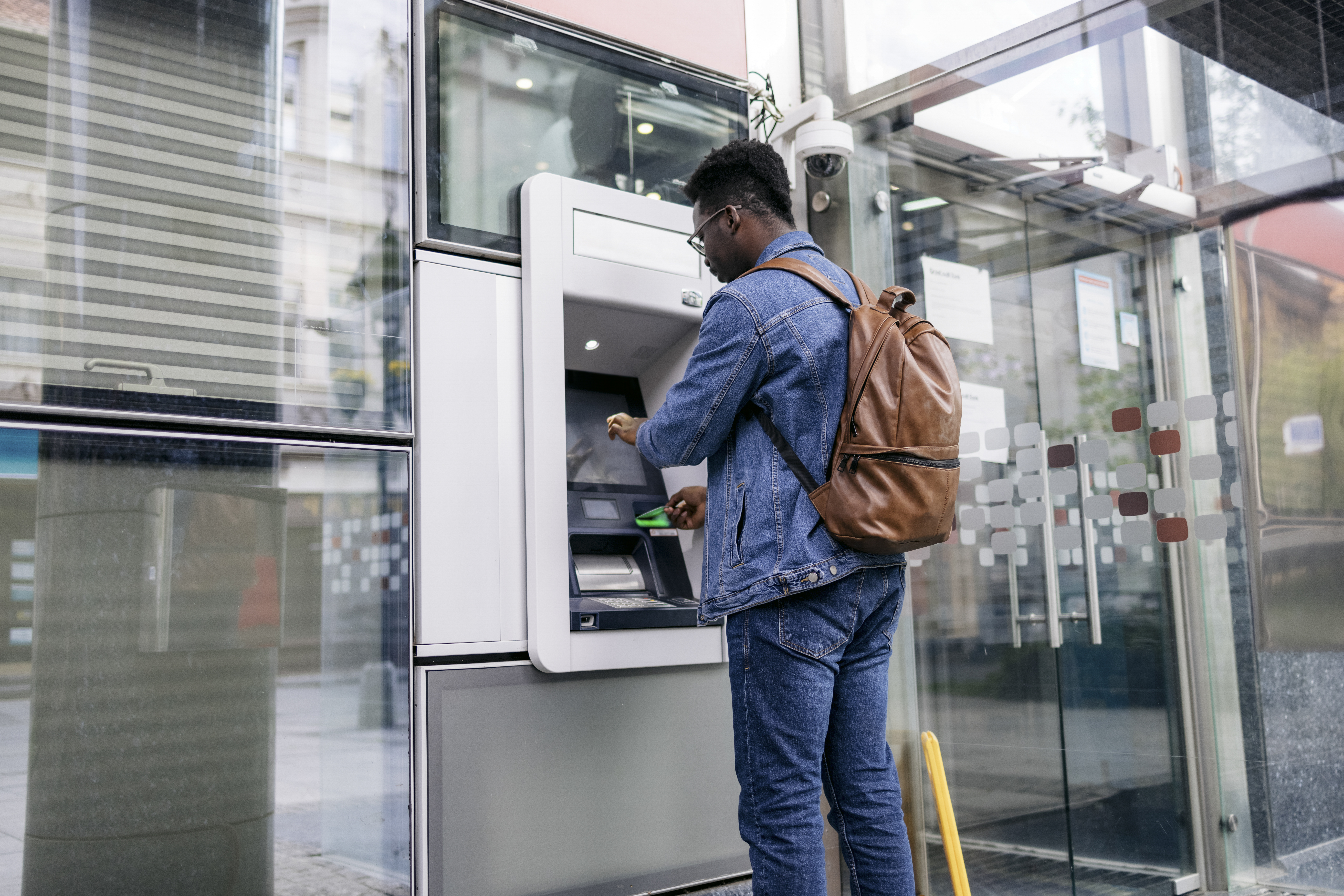 Handsome young man stopping by an ATM in the city and using a credit card to retrieve cash from his bank account